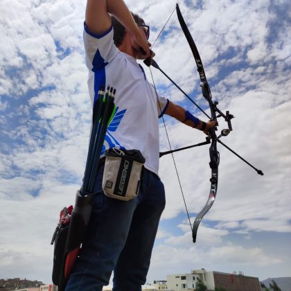 Hombre disparando en un campo abierto, tiene una camiseta blanca y un jean azul